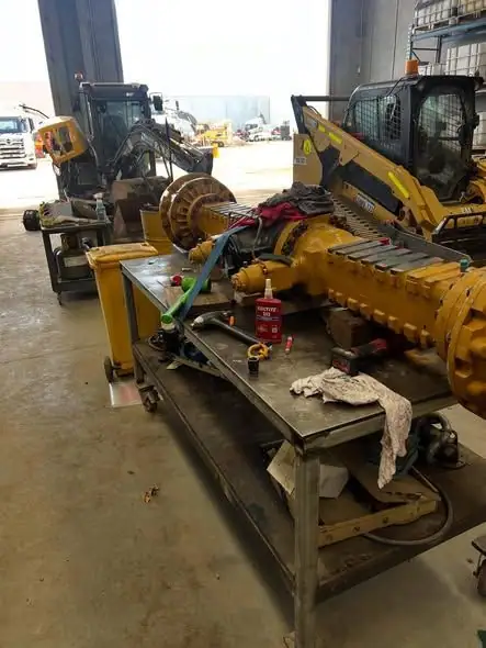 A differential on a steel workshop bench with a skid steer parked behind.