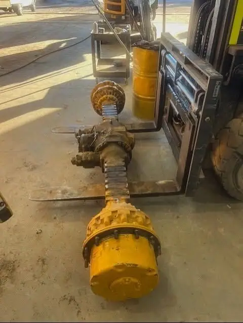A yellow differential and axle assembly lifted on forklift tines in a workshop.